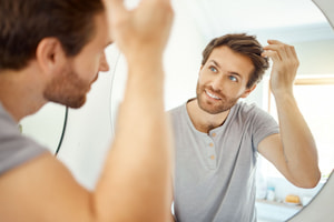 man looking in the mirror happily after receiving nutrafol treatment