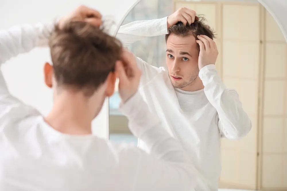 young man looking at his thinning hair line in the mirror
